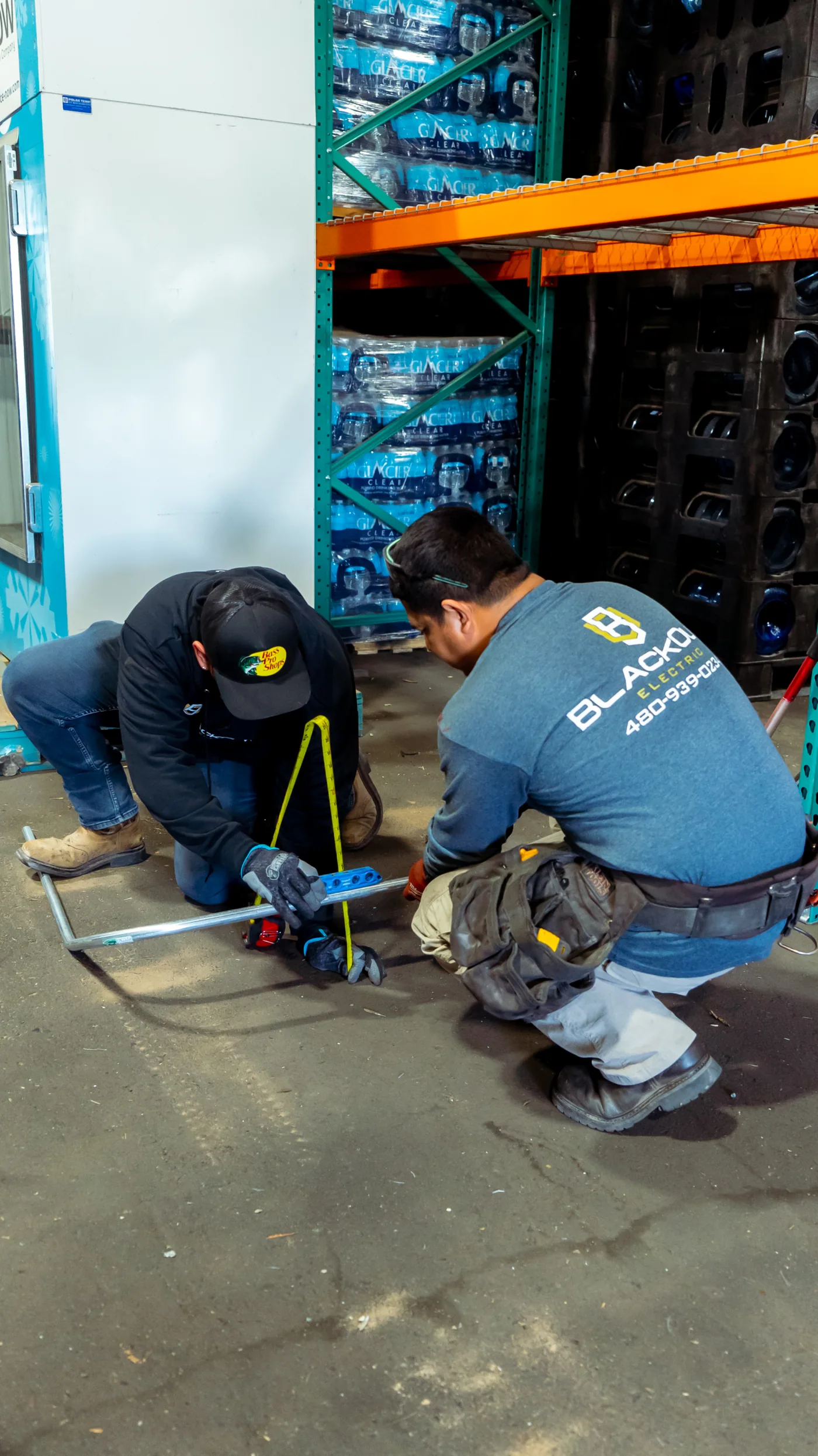 Two Blackout techs kneeling on the concrete, laying out a conduit run with a folding rule