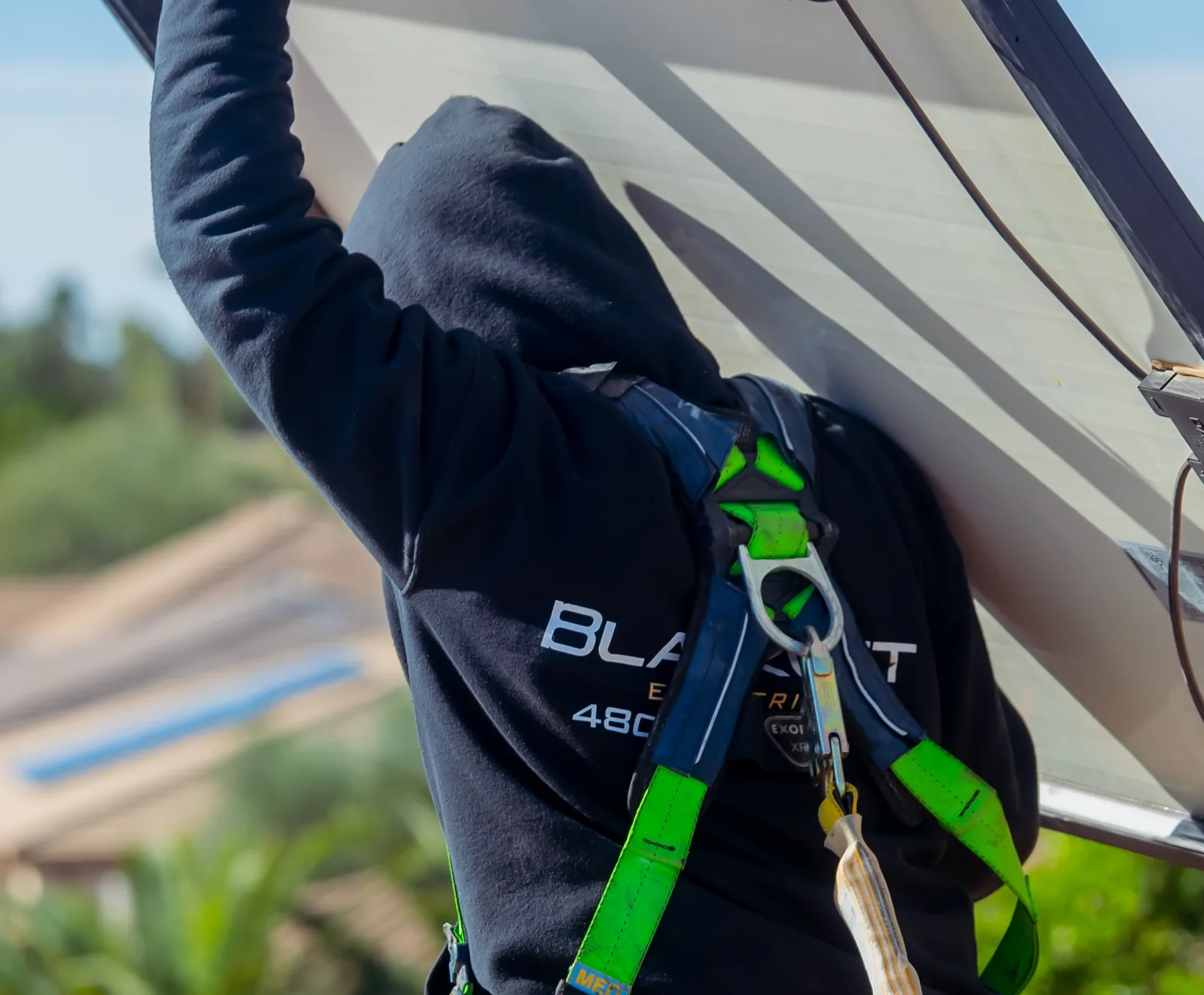 Blackout Electric technician in a harness raising a solar panel overhead during a detach