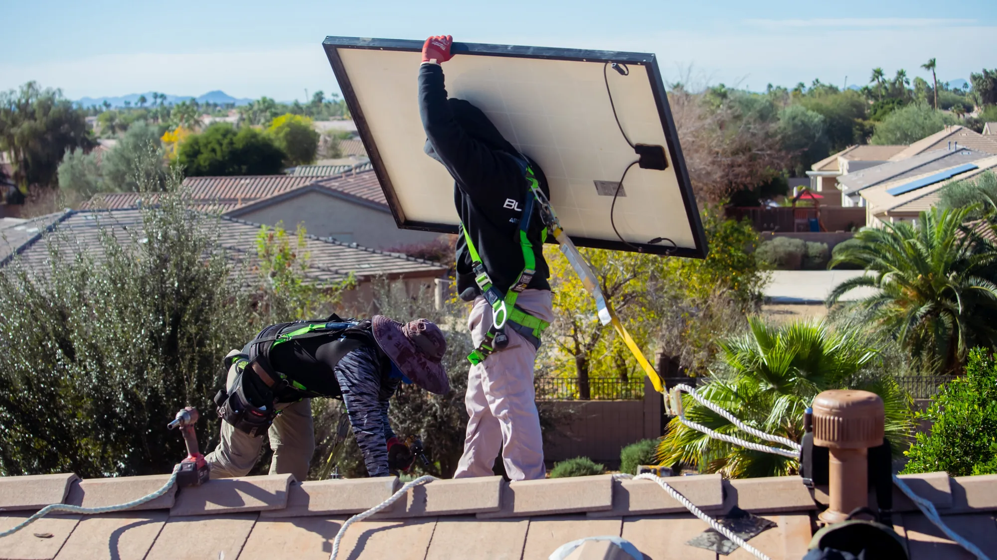 Blackout Electric technician carrying a solar panel along a roof ridge