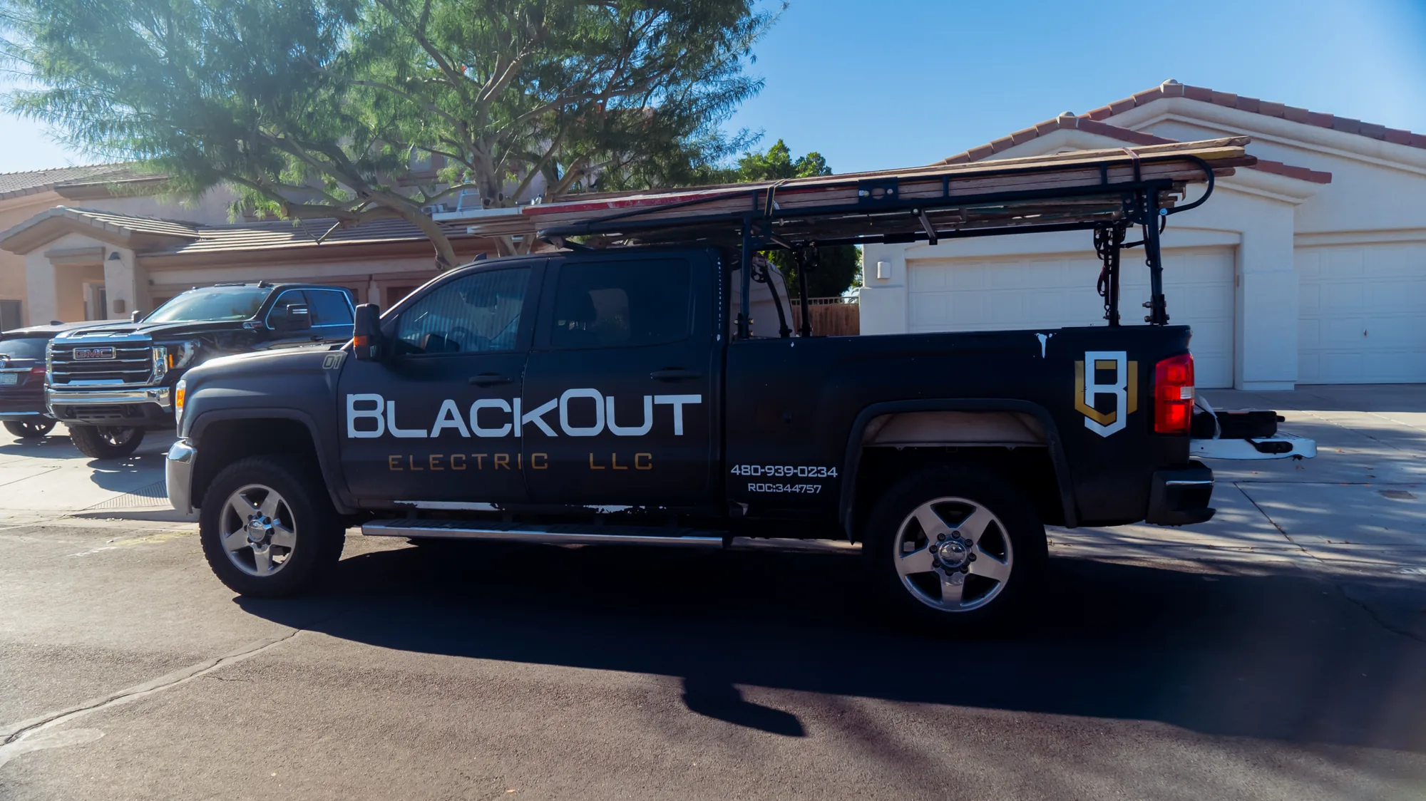 Black Blackout Electric pickup with a loaded ladder rack parked at a residential job